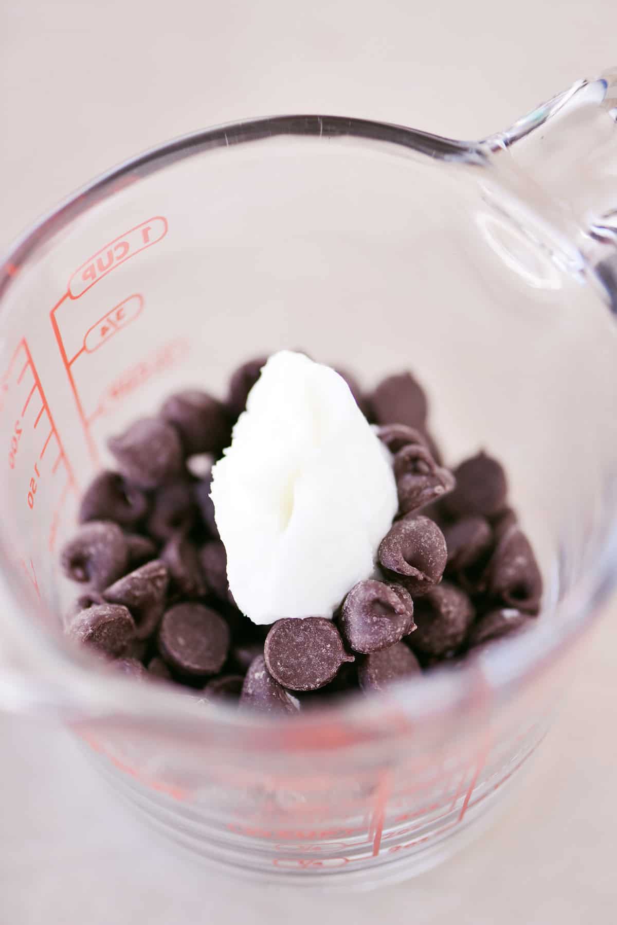 Chocolate chips and shortening in a glass measuring cup.