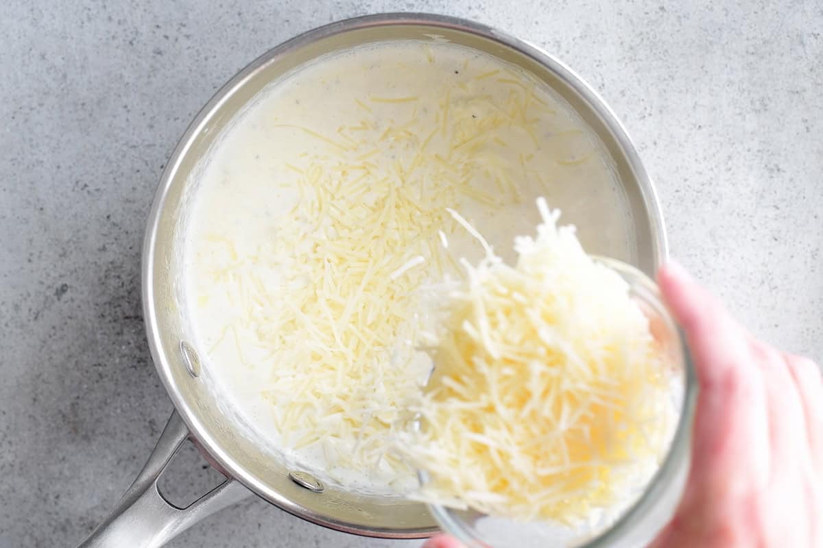 Adding parmesan to cream in saucepan.