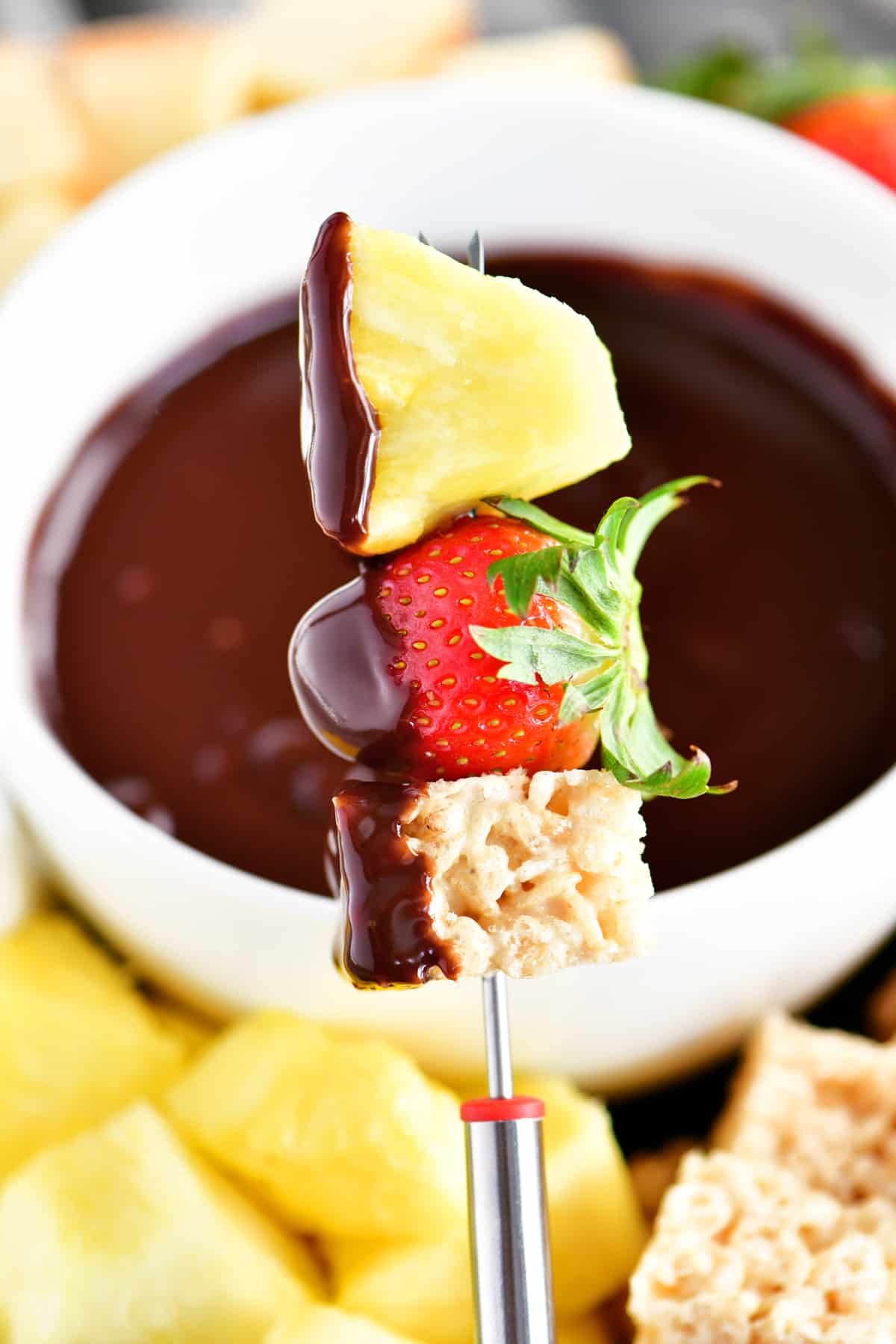 A rice crispy square, strawberry and pineapple with chocolate fondue.