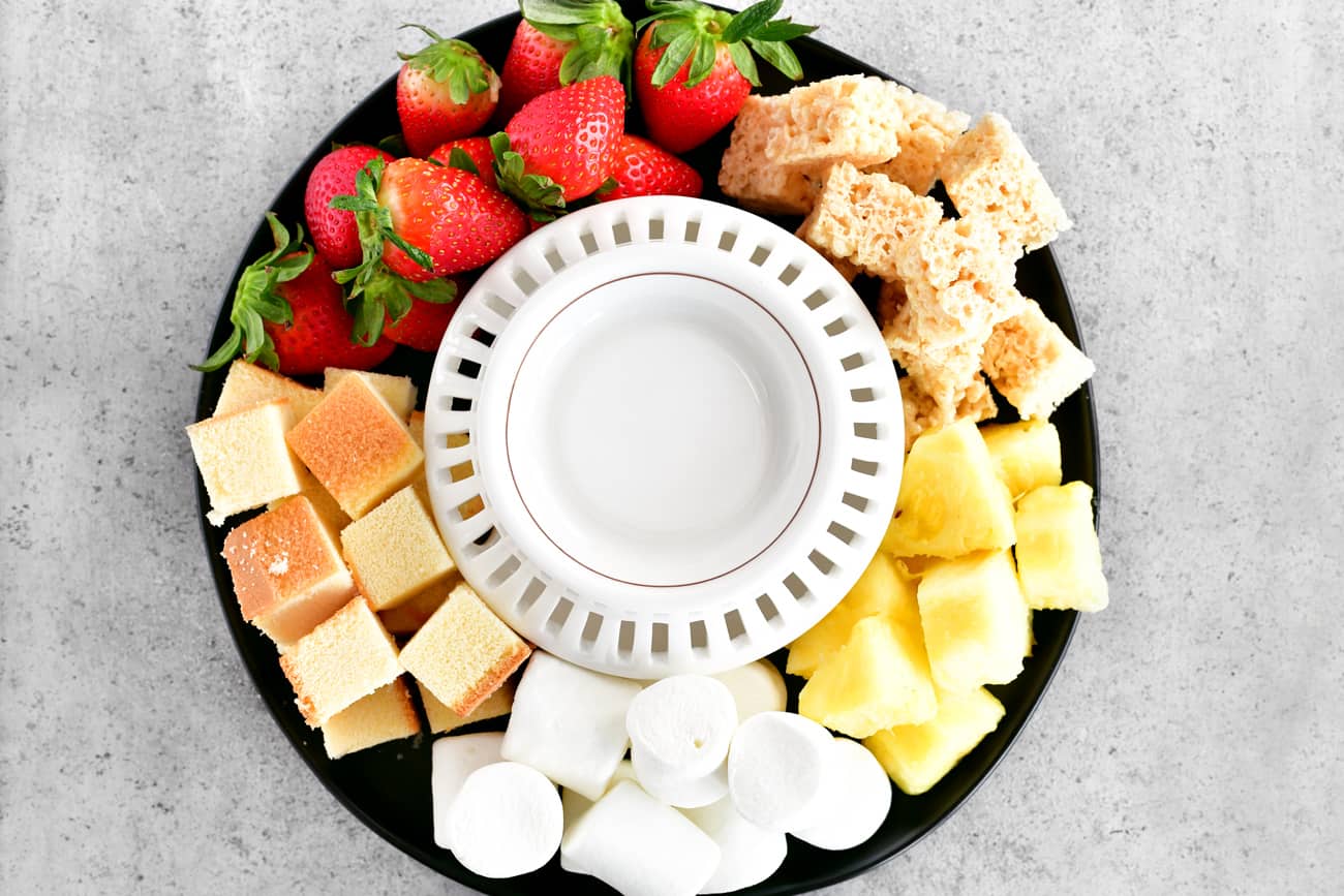 A fondue pot surrounded with fruit and sweet treats.