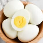 Boiled eggs in a bowl, one egg is cut in half so you can see the yolk