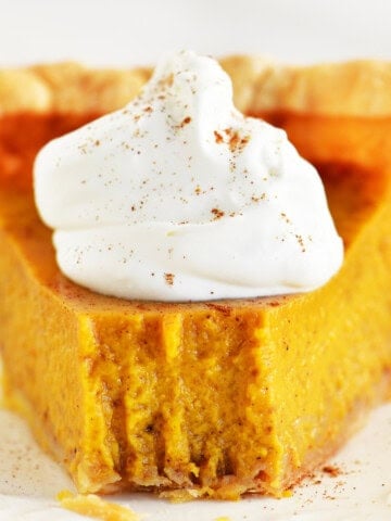 A slice of pumpkin pie with condensed milk on a white plate.