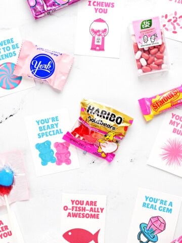 Assorted candies and free printable valentine cards for kids on a countertop.