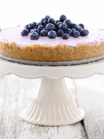 A no bake blueberry cheesecake on a white cake stand.