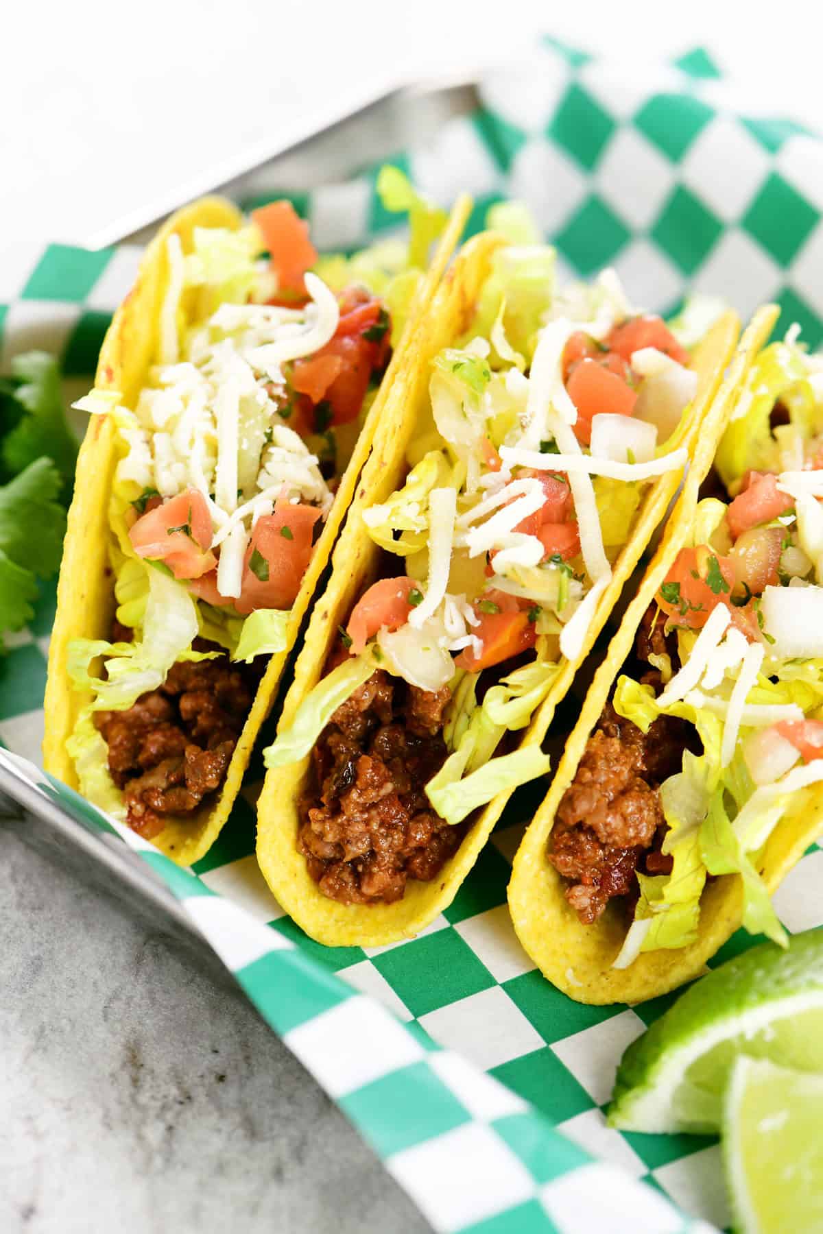 Three crock pot tacos on a tray with a green checkered liner.