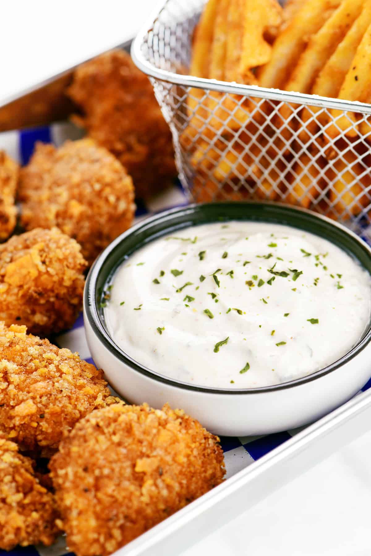 Seasoned sour cream in a small bowl on a tray with chicken nuggets and fries.