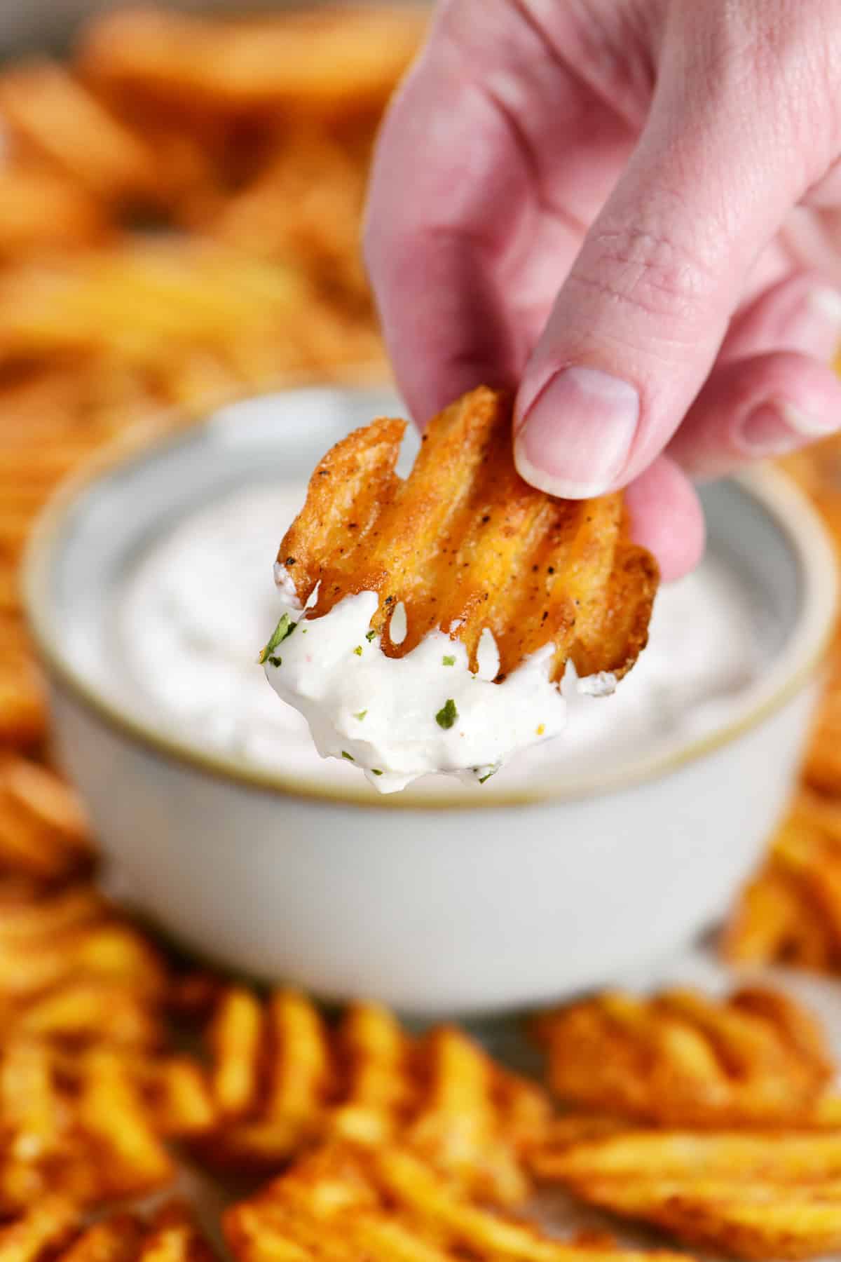A hand holding a waffle fry with seasoned sour cream on top.