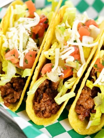 Three slow cooker tacos in a hard shell with toppings.