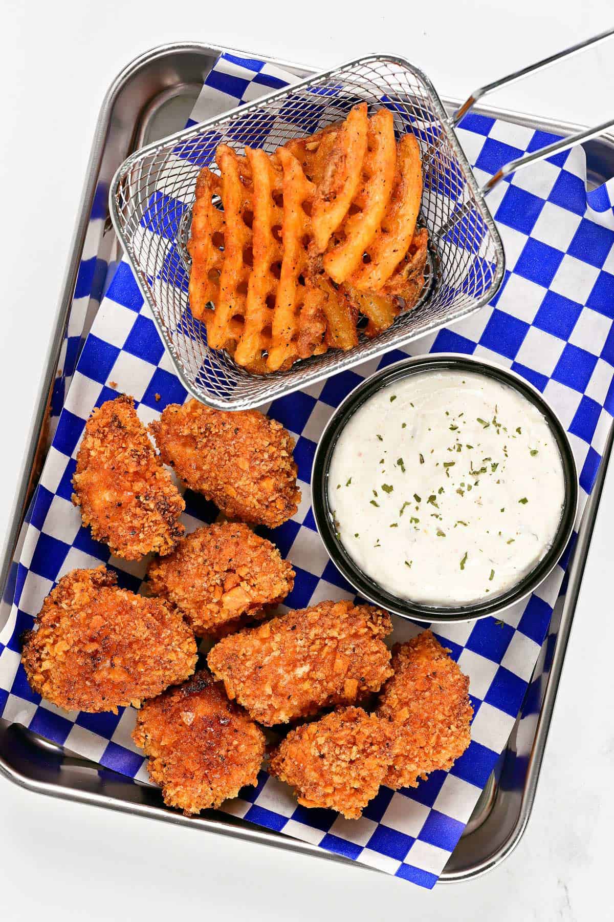 Spicy chicken nuggets, waffle fries, and dip on a checkered lined tray.