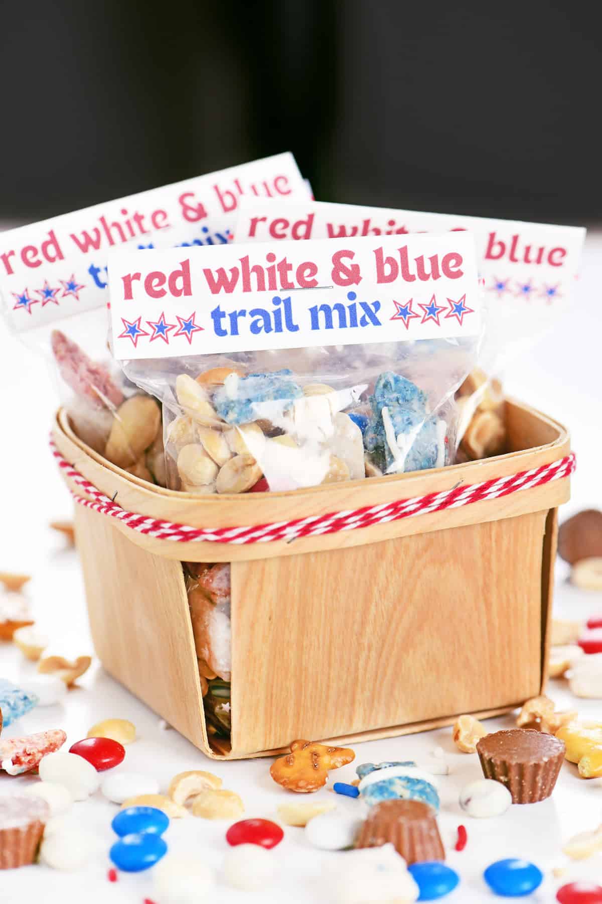 Red white and blue trail mix in labeled bags in a wooden berry basket.