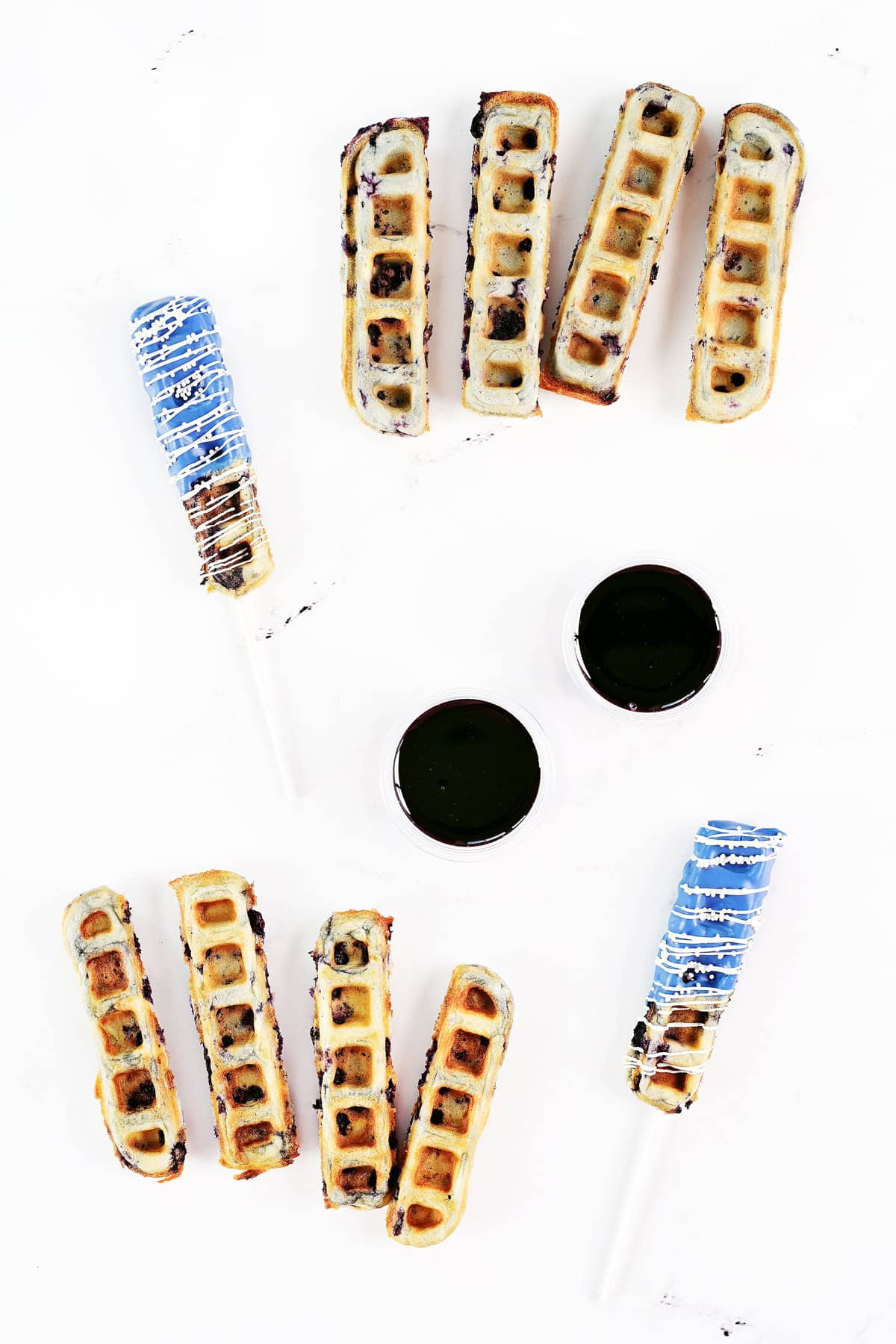 Blueberry waffle sticks and pops and blueberry syrup in cups.