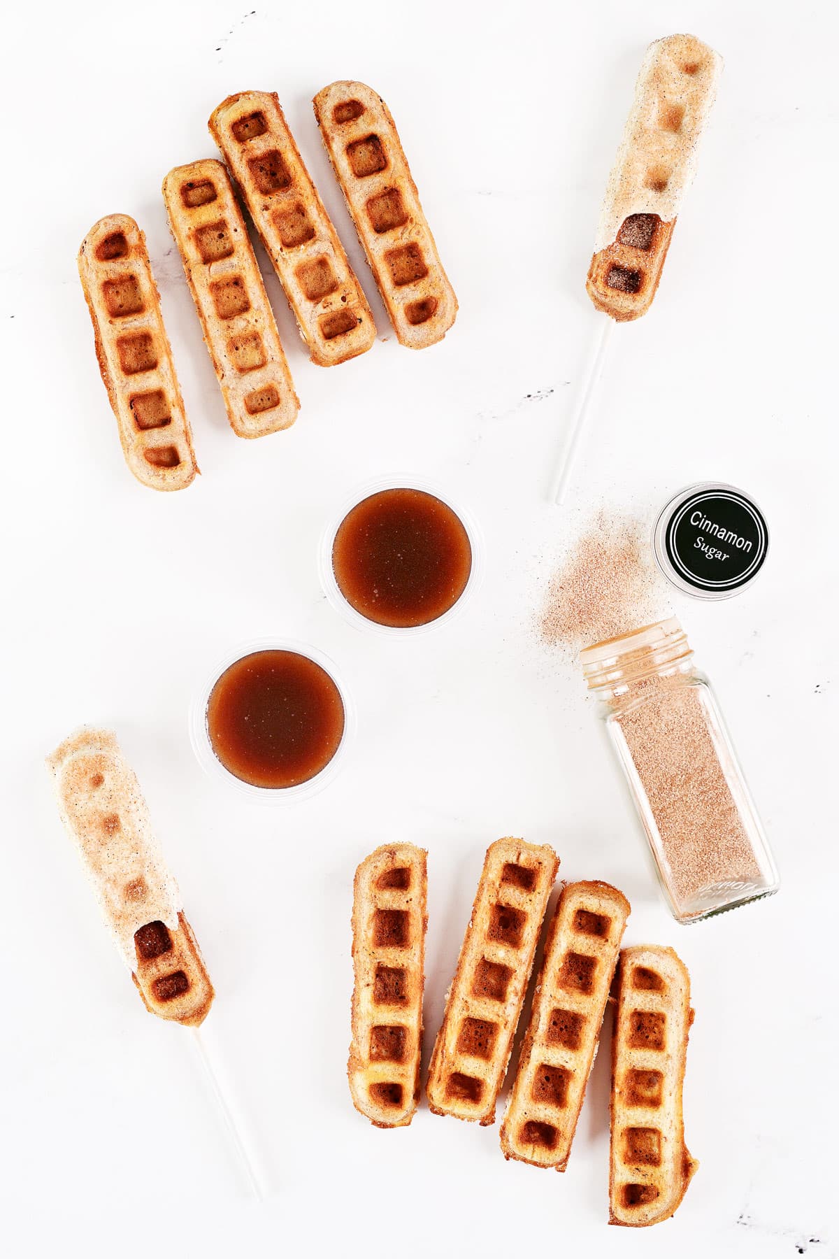 Cinnamon waffle sticks, churro waffle pops, cinnamon sugar, and cinnamon syrup in cups.