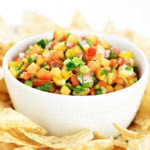 Peach salsa in a white bowl on a tray with tortilla chips.