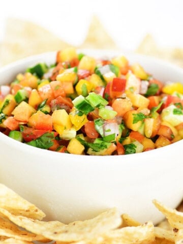 Peach salsa in a white bowl on a tray with tortilla chips.