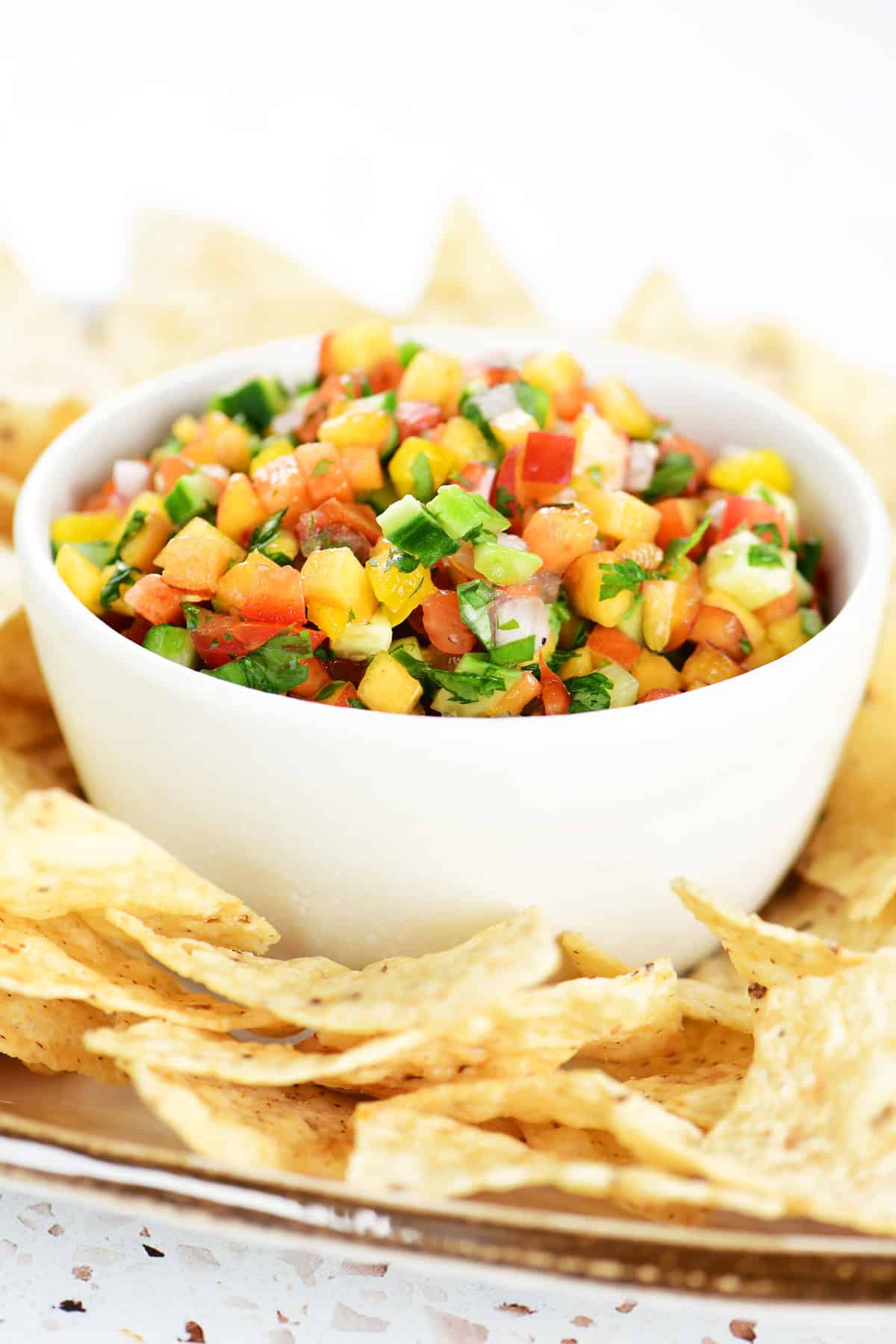 Peach salsa in a white bowl on a tray with tortilla chips.