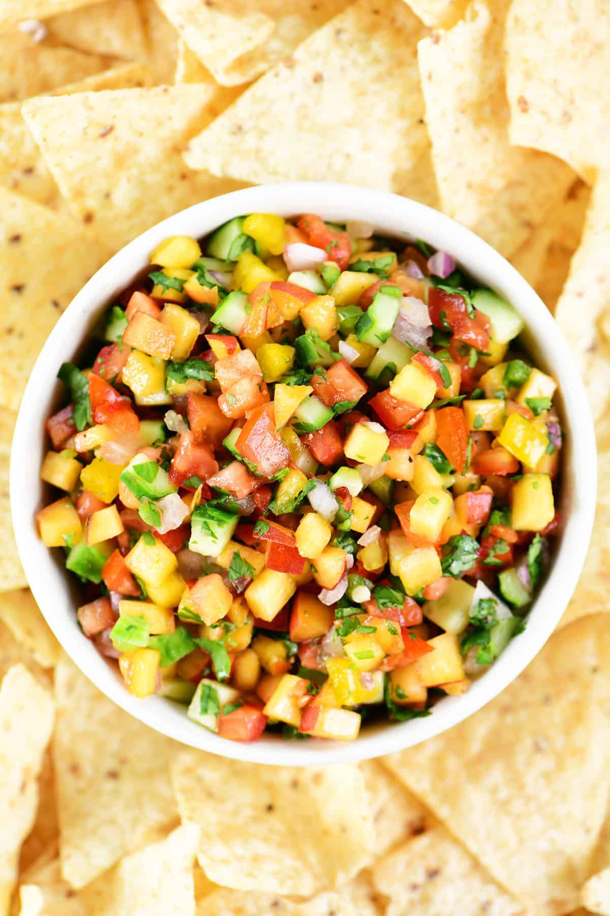 Peach salsa in a white bowl surrounded by tortilla chips.