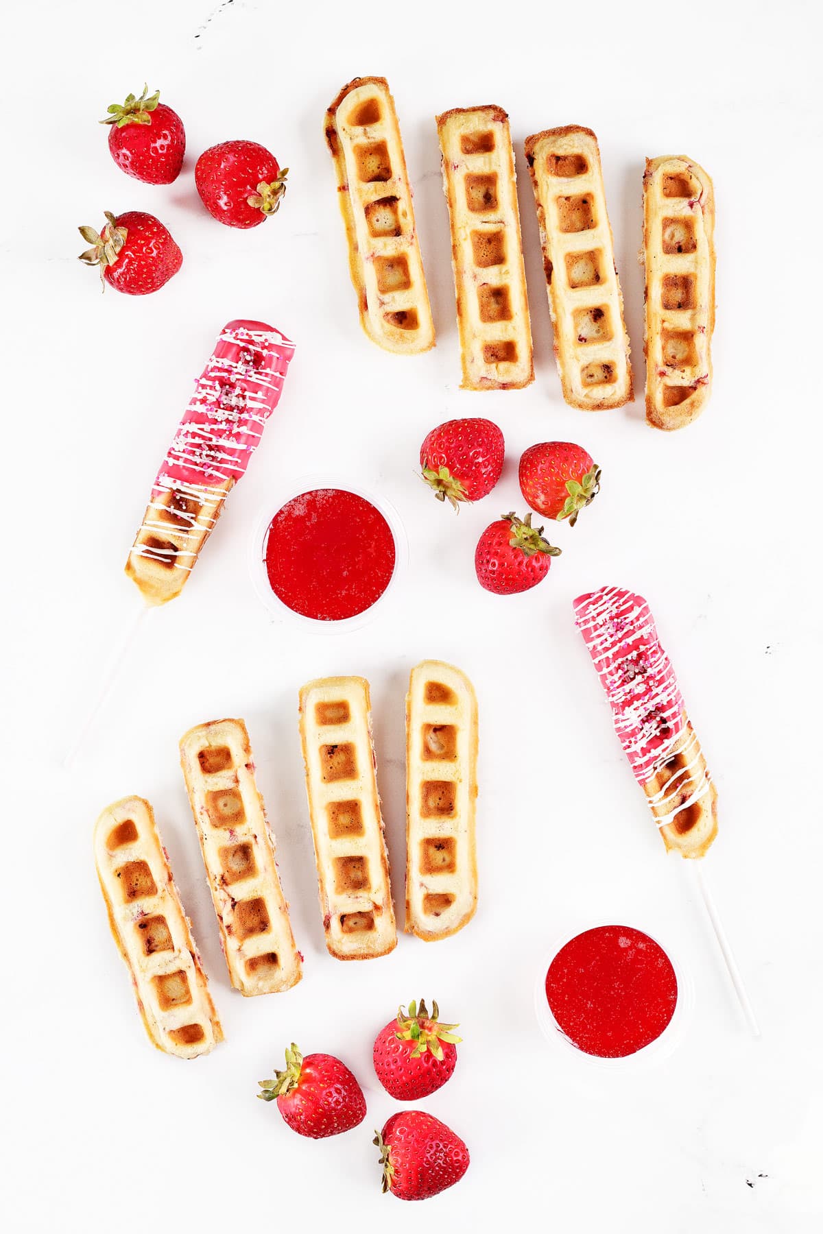 Strawberry waffle sticks, strawberry waffle pops, strawberry syrup in cups, and fresh strawberries.