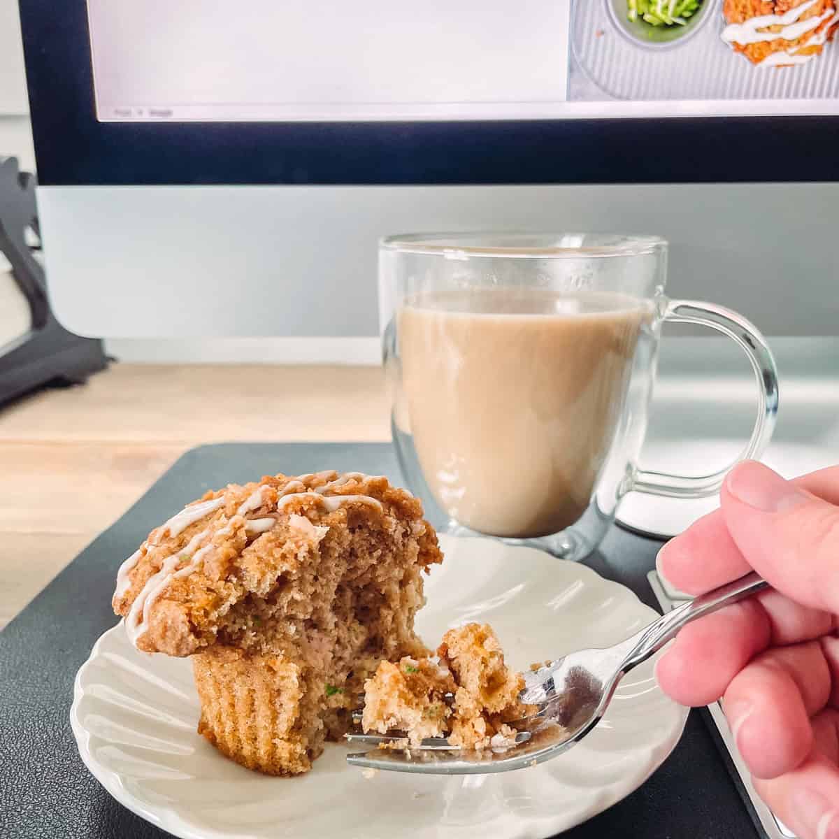 Eating a zucchini muffin with a computer in the background.