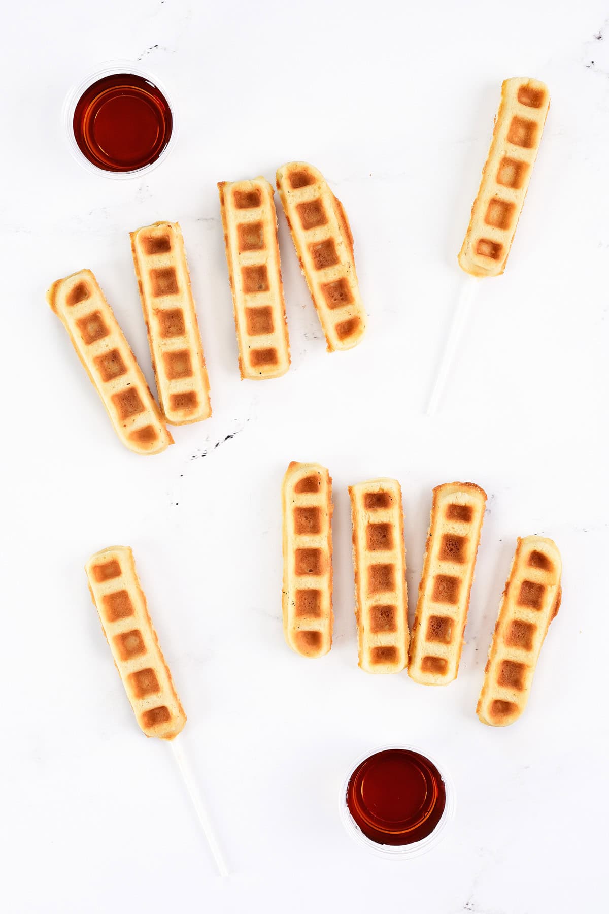 Plain waffle sticks, waffle pops, and maple syrup in cups.