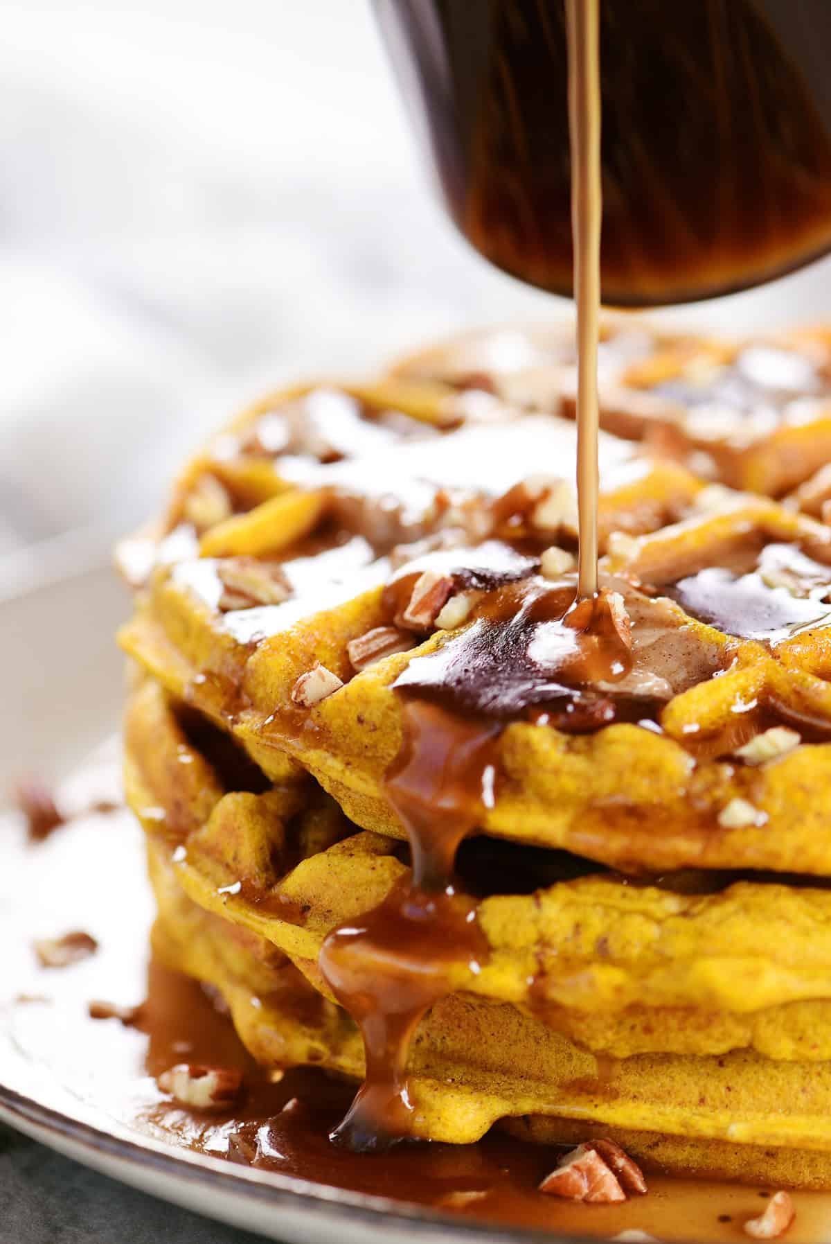 Drizzling syrup on a stack of pumpkin pecan waffles.