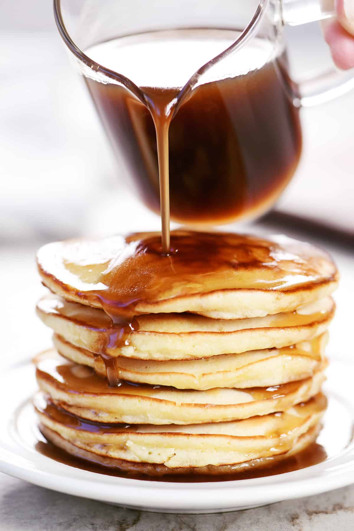 Pouring homemade pancake syrup over pancakes.