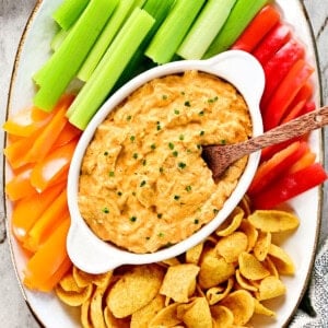 Slow cooker buffalo chicken dip on a platter with veggies and chips.