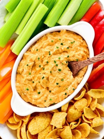 Slow cooker buffalo chicken dip on a platter with veggies and chips.