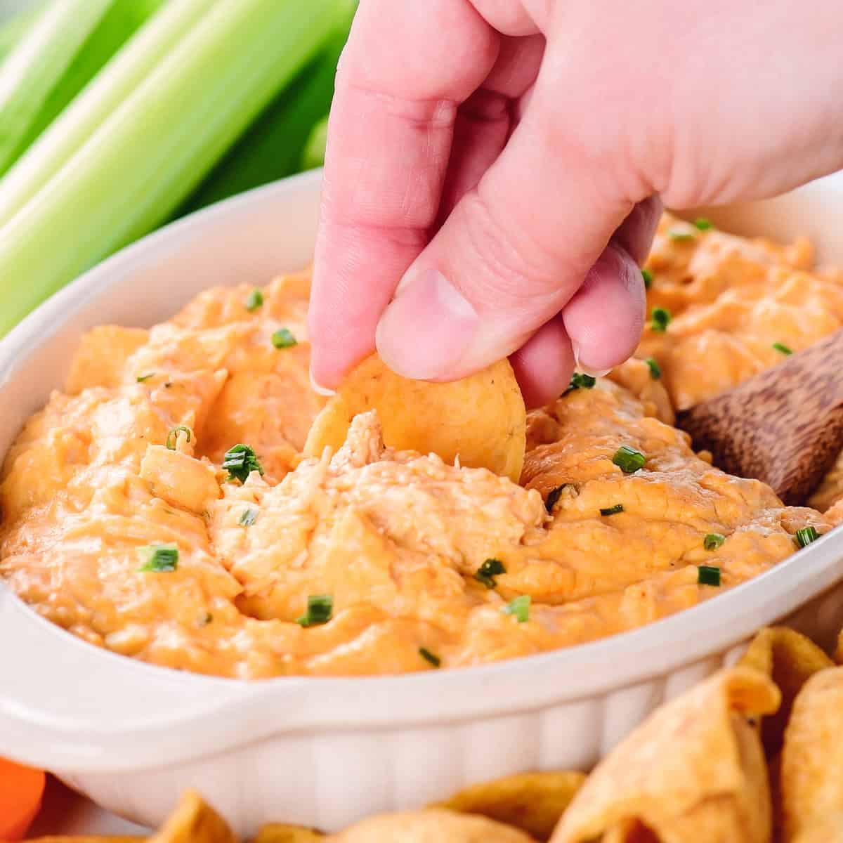 A hand scooping buffalo chicken dip with a Fritos.