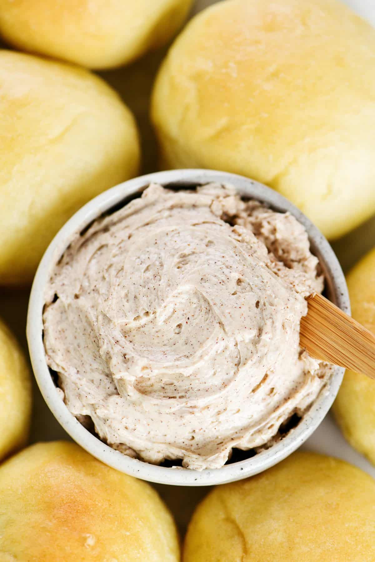 Cinnamon butter in a bowl surrounded by dinner rolls.