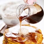 Pouring cinnamon syrup from a pitcher onto pancakes.