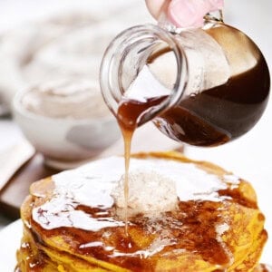 Pouring cinnamon syrup from a pitcher onto pancakes.