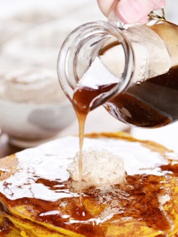 Pouring cinnamon syrup from a pitcher onto pancakes.