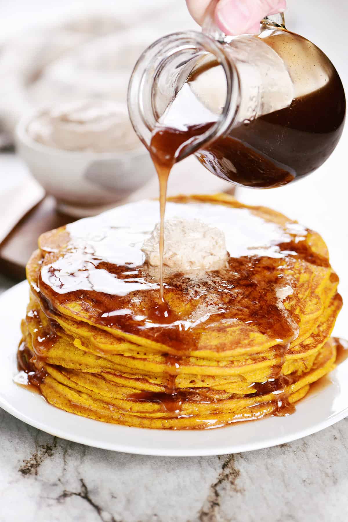 Pouring cinnamon syrup on a stack of pumpkin pancakes.