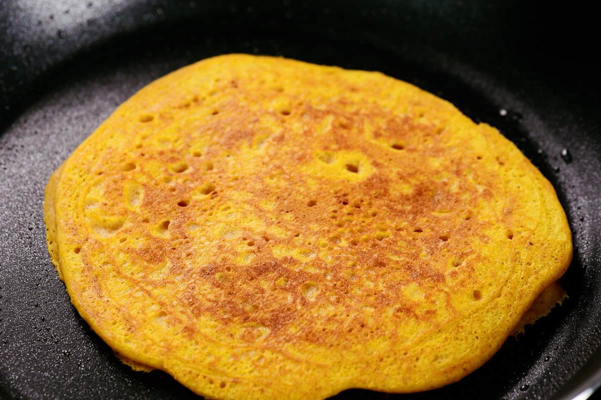 A golden brown pumpkin pancake in a skillet.