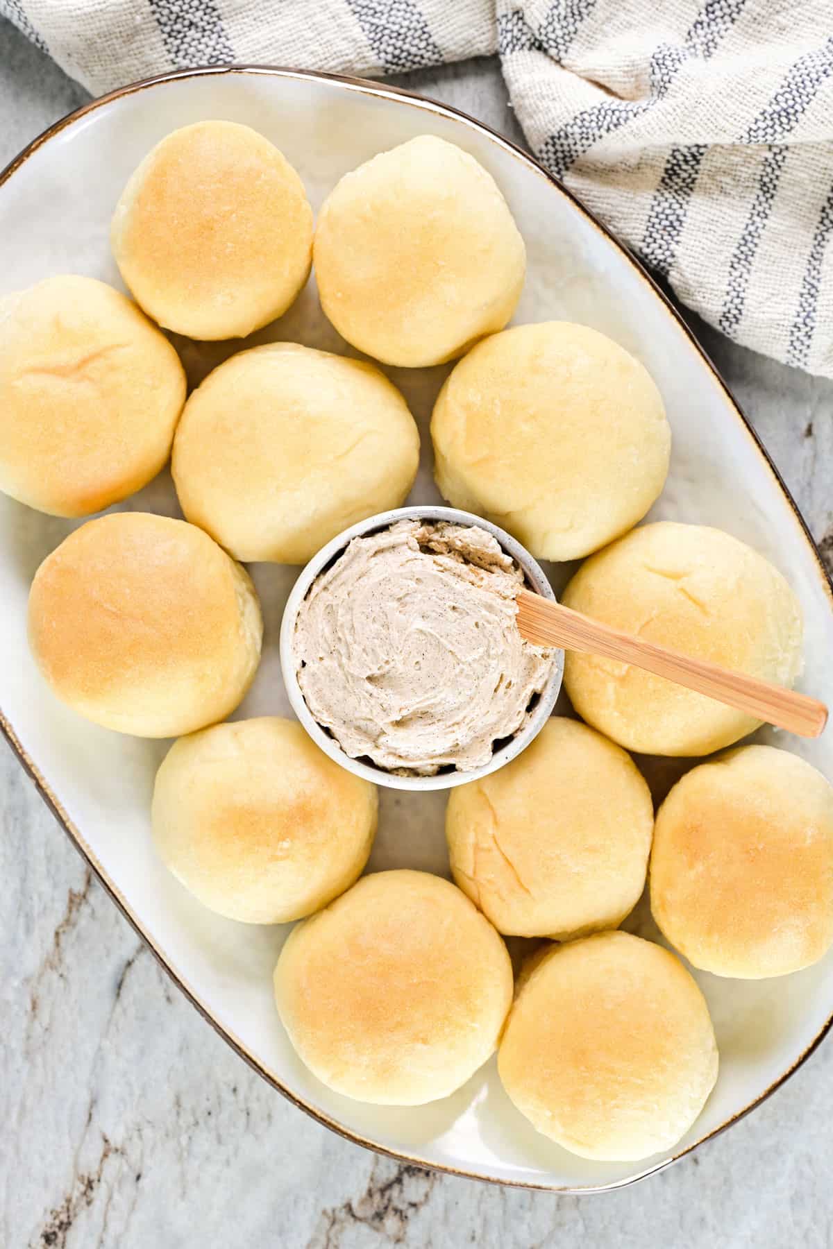 A platter holding whipped honey cinnamon butter and dinner rolls.