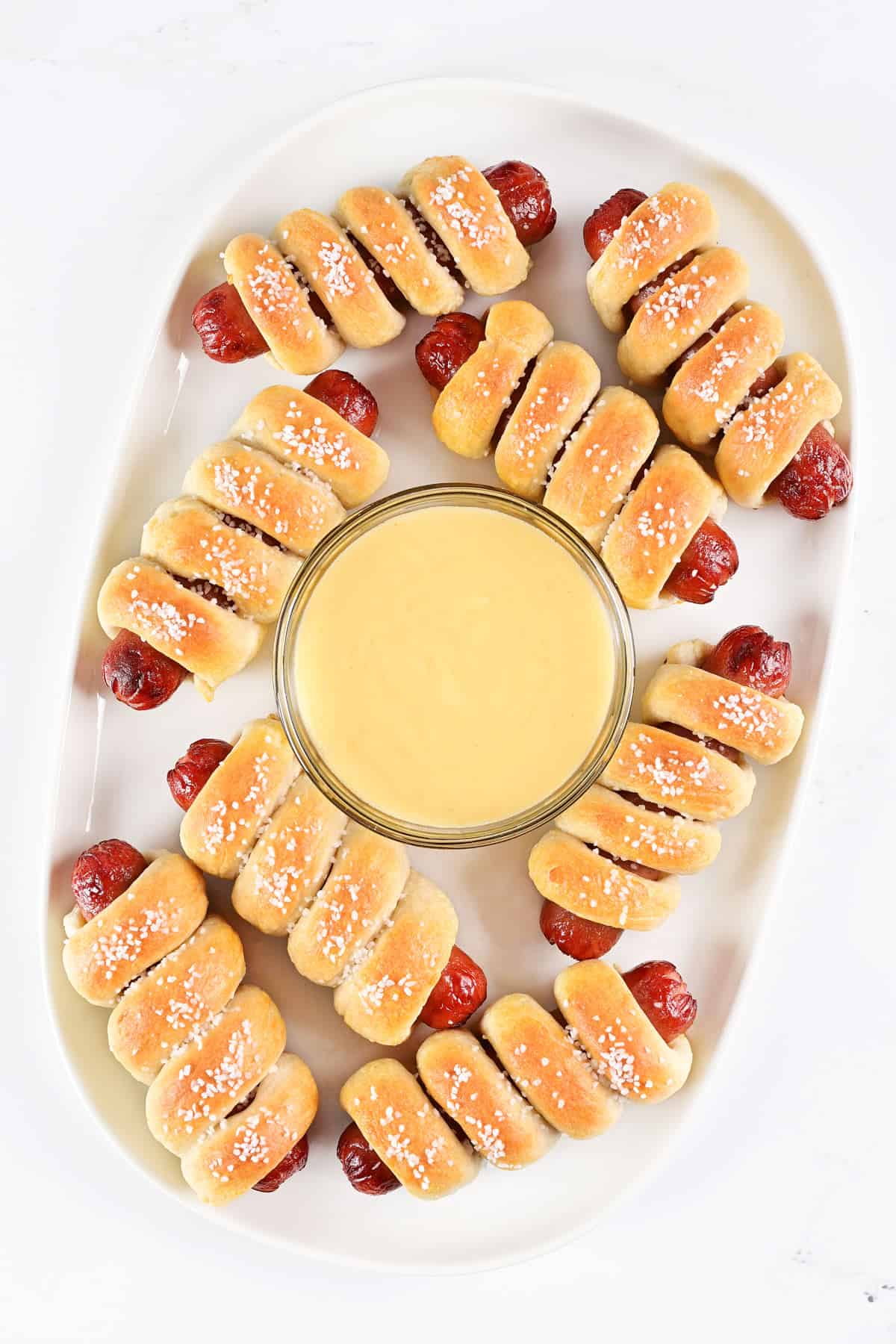 Two ingredient dough pretzel dogs on a platter with cheese dip.