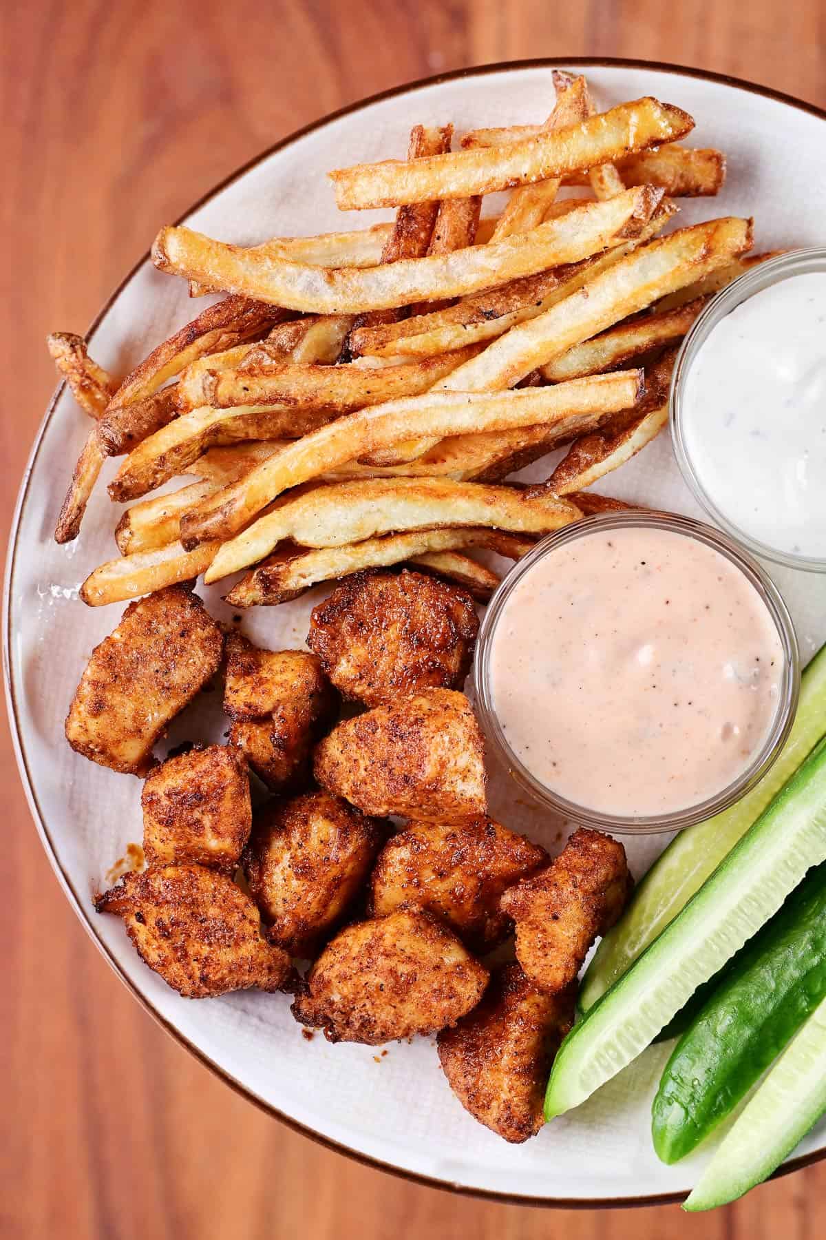 Air fryer chicken bites, french fries, cucumber, and dip on a plate.