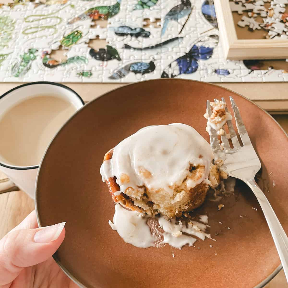 A no yeast cinnamon roll on a plate with a puzzle on the table.