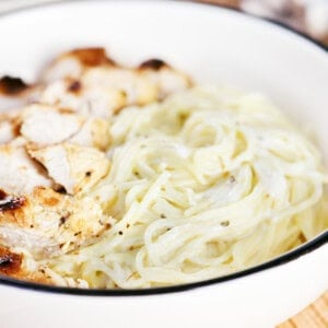 Angel hair pasta with a creamy herb sauce in a bowl with sliced chicken.