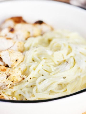 Angel hair pasta with a creamy herb sauce in a bowl with sliced chicken.