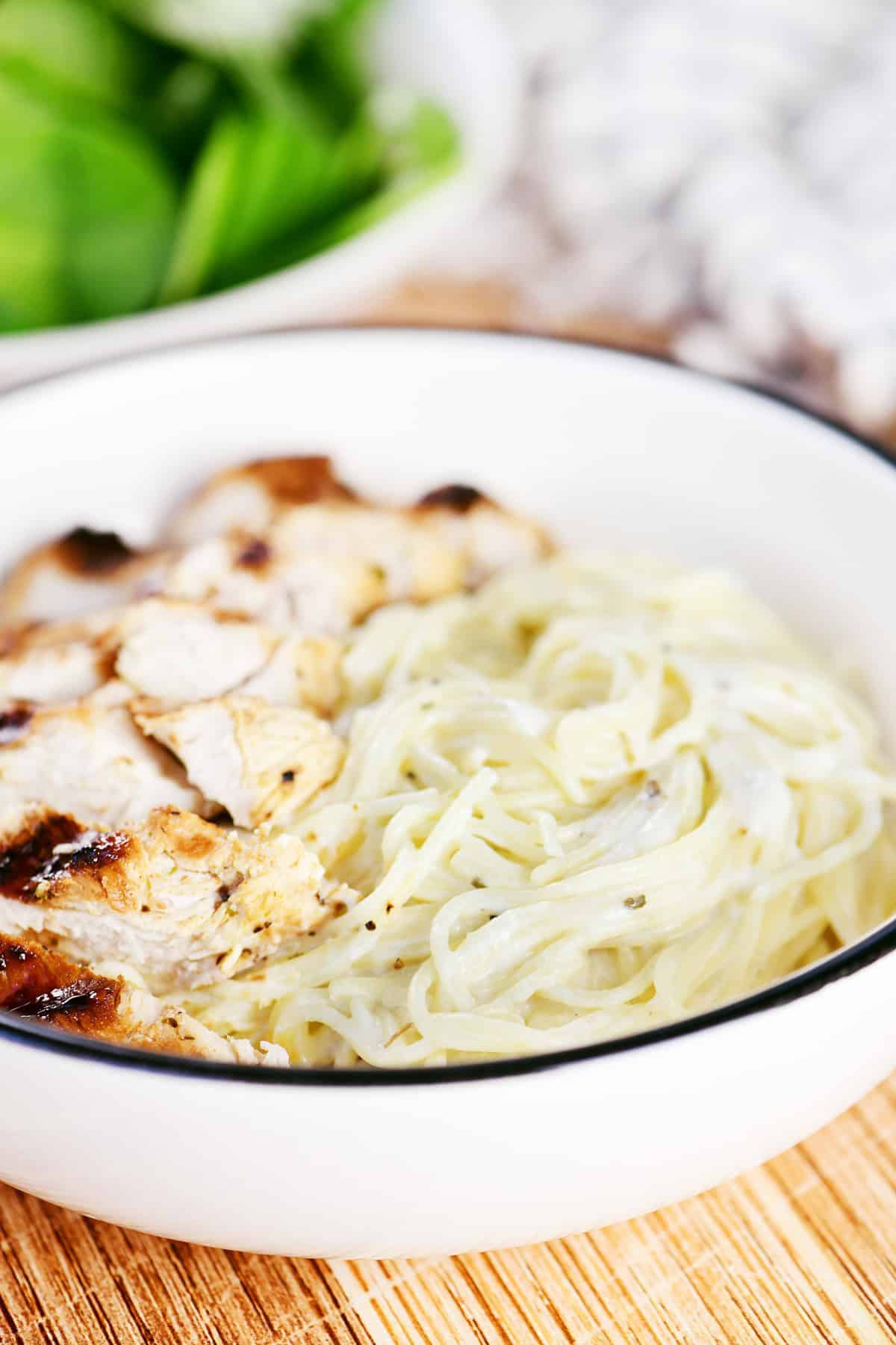 Angel hair pasta with a creamy herb sauce in a bowl with chicken.