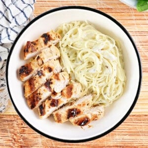 Angel hair pasta with a creamy sauce in a bowl with sliced chicken.