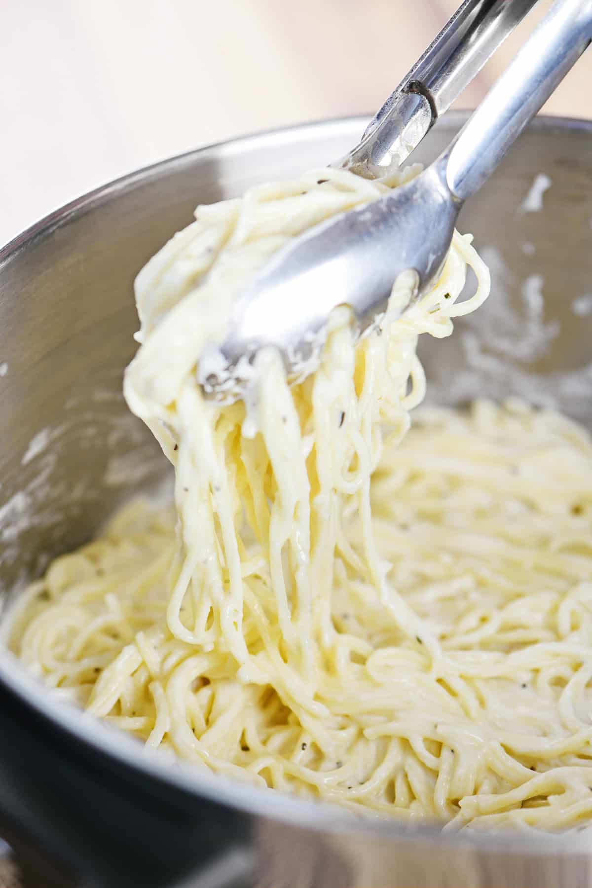 Using tongs to get angel hair pasta with creamy herb sauce.